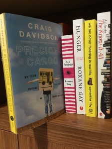 Image displays a row of book on a wooden bookshelf with Precious Cargo pulled out and tilted over the edge.